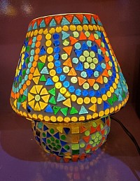 Lampe Mosaïque Artisanale – 50,00 €  Son design géométrique aux couleurs vives (bleu, vert, jaune, orange, rouge) crée une ambiance chaleureuse et artistique dès qu’elle s’illumine.  Hauteur 24 cm × Largeur 22 cm