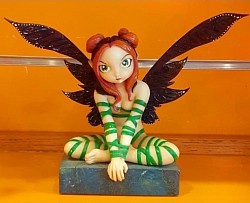 Ma Fée Enchantée – 65,00 € Plongez dans l’univers mystique de cette fée unique, assise en méditation sur son socle de pierre. Avec ses ailes sombres finement texturées et ses rubans verts enroulés autour de son corps, elle incarne la magie, la force intérieure et la sérénité. Détails magiques : - Création artisanale, pièce unique - Hauteur : environ 20 cm - Rubans verts, ailes texturées, coiffure en double chignon - Socle en ardoise, ambiance féerique garantie